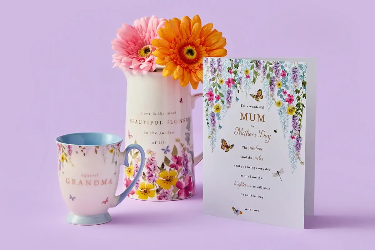 A colourful Mother’s Day set featuring a floral MUM card, a tulip‑patterned mug with matching coaster, a tall floral tumbler, and a single red tulip arranged on a pastel purple background.